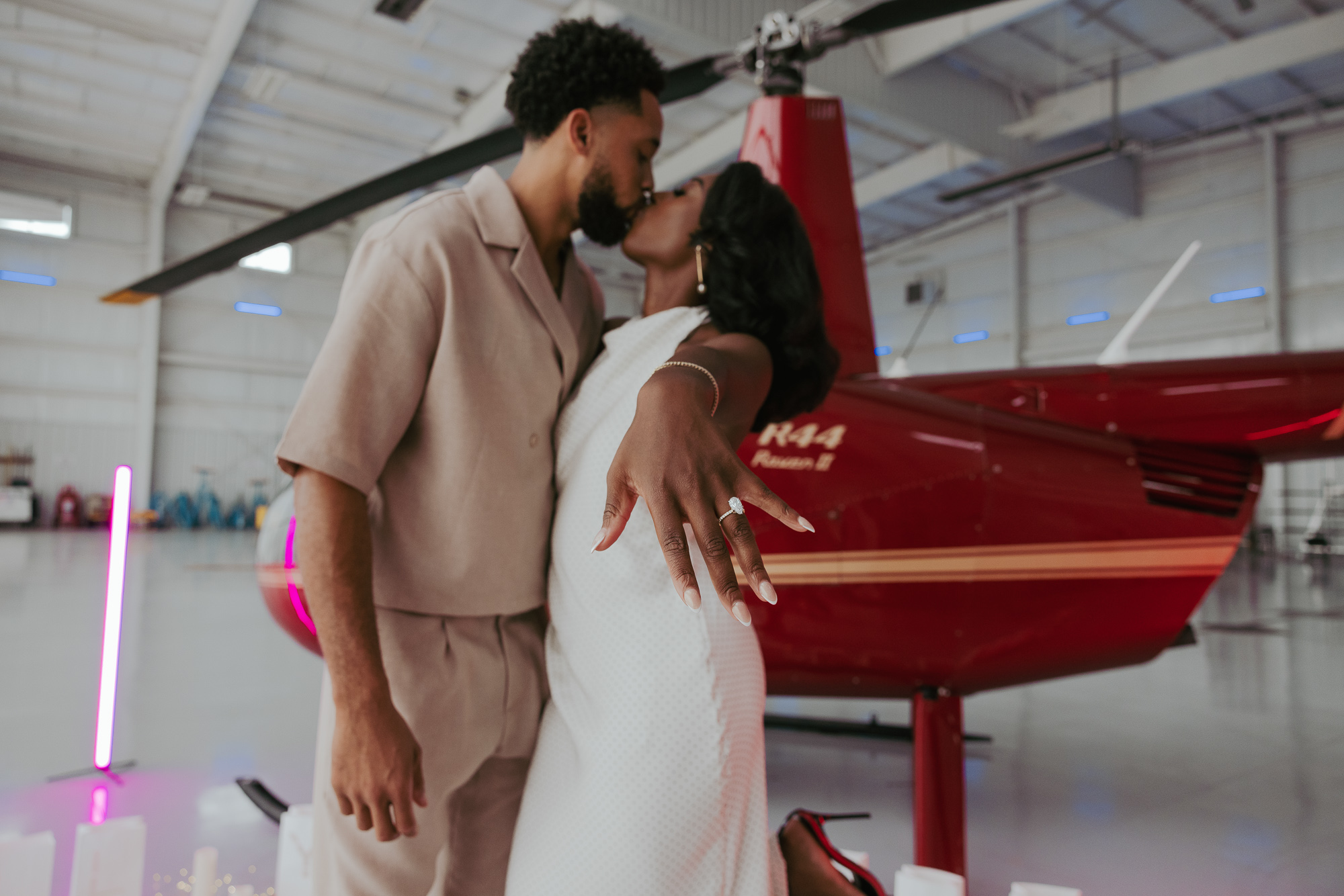 Newly engaged couple kissing in a hangar, showing an engagement ring