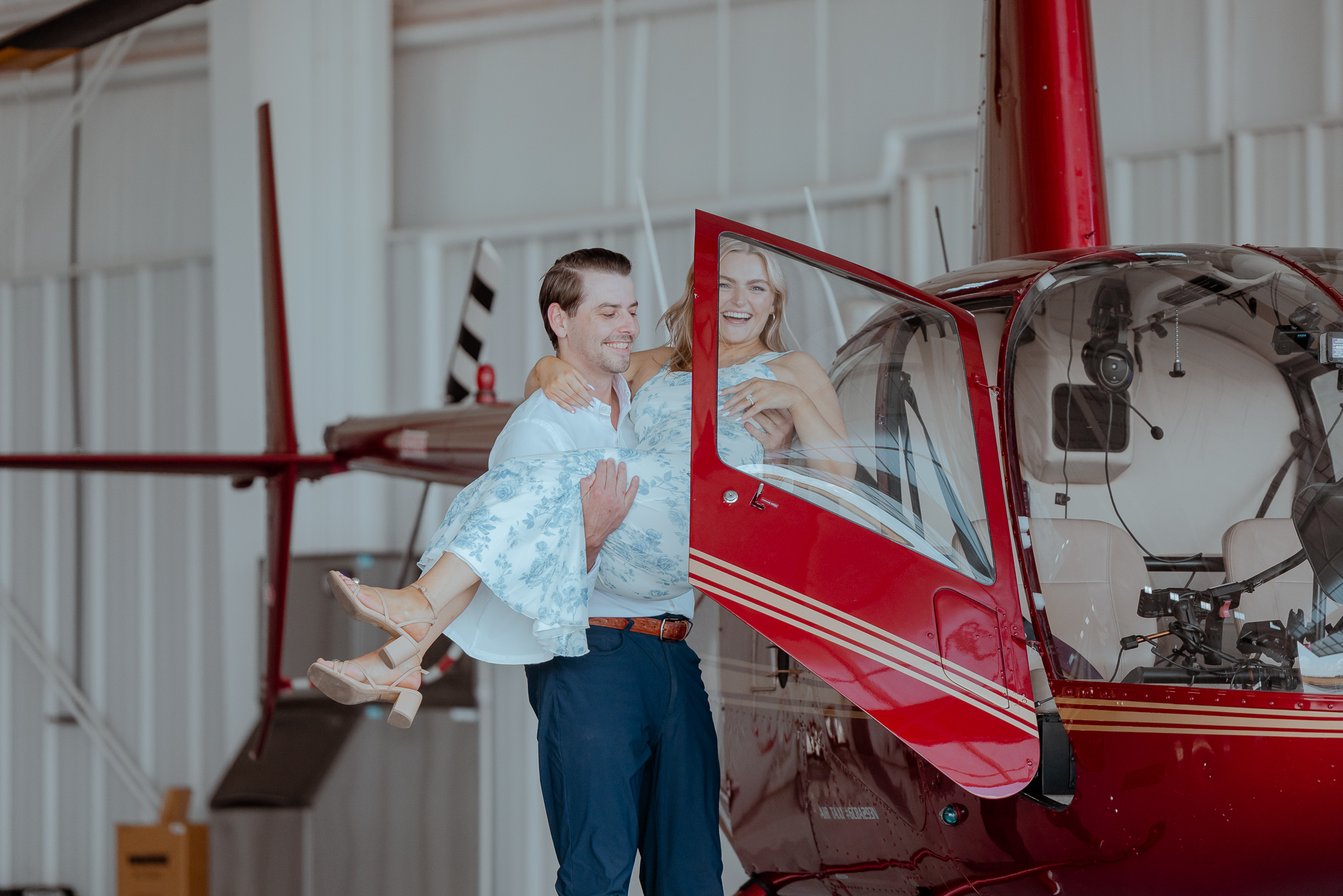 Celebrating couple in front of a red helicopter after a hangar proposal