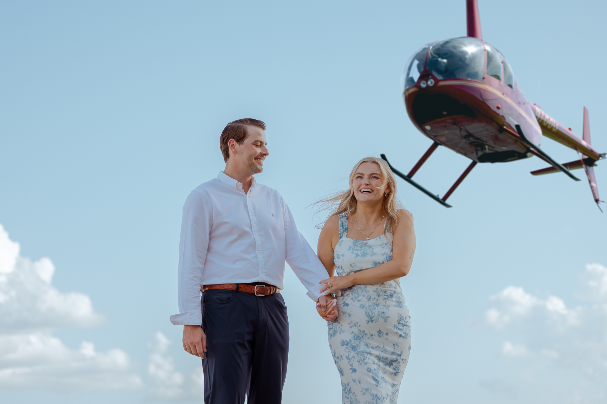 Couple walking together with a helicopter overhead after their proposal flight